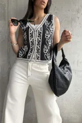 Chaleco negro con bordado floral blanco, escote en V, cierre frontal con botones y ribete de encaje.