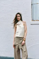 Pantalón de tiro medio con detalle de pareo superpuesto en la cintura y cierre de lazo lateral. Presenta pierna ancha y corte recto.