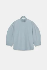 Camisa de algodón con cuello alto y mangas abullonadas por debajo del codo. Presenta cierre frontal con botones ocultos bajo solapa.