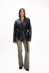 Chaqueta de cuero sintético negro con solapas anchas y cinturón del mismo material para atar en la cintura, de mangas largas y corte holgado.