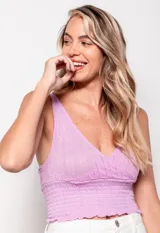 Top tejido color lila, sin mangas, con escote en V profundo y diseño cruzado en frente y espalda. Presenta calados y detalle de punto smock en la parte inferior.