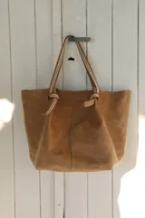Bolso tipo shopper de cuero color tostado, con diseño de costuras visibles en las asas y detalle de nudos en la unión de las mismas con el cuerpo del bolso.