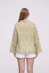 Blusa de algodón con estampado de hojas en tonos verdes sobre fondo blanco, cuello camisero, cierre frontal con botones y mangas largas.