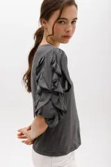 Remera color beige con mangas cortas y volados con borde naranja.