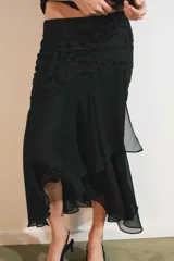 Falda midi negra de tiro medio con superposición de tejido transparente con diseño estampado y aplicación de abalorios a tono. Presenta bajo asimétrico con volantes y forro interior negro.