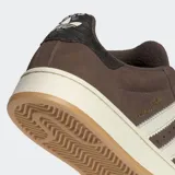 Championes Adidas Campus 00s de color marrón, confeccionados en cuero con las icónicas tres tiras dentadas en color blanco. Presentan una suela de caucho en tono crema y detalles en dorado, con un diseño inspirado en la cultura urbana y el skate de los años 2000.
