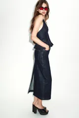 Top de mezclilla (denim) azul oscuro con cuello halter que se anuda en la espalda, escote pronunciado en pico y bajo abullonado con elástico. Presenta pespuntes contrastantes en color rojo.