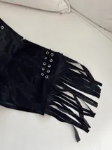 Short negro de tiro bajo con flecos en los laterales y detalle de cordones cruzados con ojales metálicos.