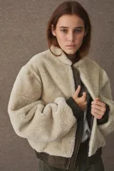 Campera tipo bomber de textura afelpada en color beige, con cierre frontal, cuello redondo y puños elásticos en color verde oliva oscuro.
