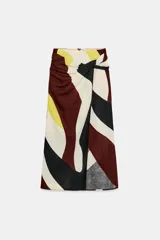Falda midi de corte cruzado con diseño tipo pareo, presenta un nudo decorativo en la parte delantera y cierre de cremallera oculta en la espalda. El tejido cuenta con un estampado geométrico abstracto en tonos bordó, negro, amarillo y crema.