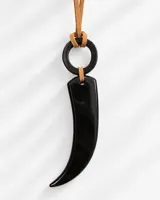 Collar largo con dije en forma de colmillo de resina negra, un anillo de resina también negro y cordón de gamuza marrón claro.