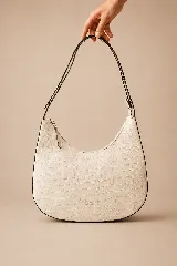 Cartera hobo de cuero color marfil con textura en relieve efecto cocodrilo, diseño de media luna y correa ajustable para el hombro.