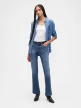 Jean de corte bootcut y tiro bajo, en color azul oscuro con acabado lavado. Presenta diseño de cinco bolsillos, cierre frontal con botón y cremallera, y costuras reforzadas en el ruedo.