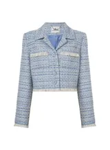 Chaqueta corta de tweed celeste con detalles en blanco y dorado, de corte sastre, con solapas de pico, cierre frontal con botones, bolsillos delanteros y terminaciones con flecos.
