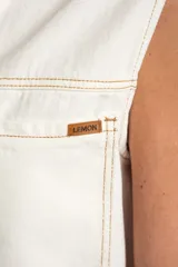 Chaleco de denim blanco con diseño sin mangas, cuello camisero, bolsillos frontales con solapa y cierre de botones metálicos con detalle de ribete ondulado en contraste.