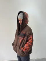 Campera reversible con cierre frontal. Un lado confeccionado en algodón color marrón con estampa plastisol en color naranja, bordados con apliques y capucha. El otro lado confeccionado en tela polar de pelo largo color negro con capucha.
