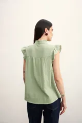 Camisa color amarillo pálido con textura arrugada, cuello mao con volados, cierre frontal con botones y mangas cortas con volados.