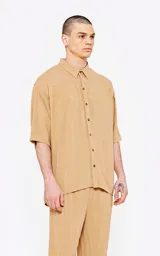 Camisa de corte oversize, color beige, con cuello clásico, cierre frontal de botones y mangas cortas. Confeccionada en tejido de lino.