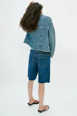 Bermuda de denim azul de tiro medio y corte relaxed, con diseño de cinco bolsillos y bajo desflecado. Cuenta con cierre frontal de cremallera y botón metálico.