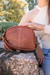 Bandolera marrón de cuero con correa larga regulable, cierre metálico y llavero de cinta.