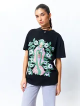 Remera negra de manga corta, corte oversize, con estampado frontal de una figura femenina de estilo asiático rodeada de flores blancas y verdes.