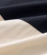 Campera cortavientos deportiva de Ashua, con diseño bicolor en negro y blanco. Presenta capucha integrada ajustable, cierre frontal con cremallera, mangas largas con puños elásticos y cintura elástica. Confeccionada en poliamida con forro de poliéster.