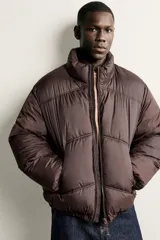 Cazadora acolchada tipo puffer de corte relajado, color negro, con cuello subido, cierre frontal de cremallera y bolsillos laterales con cierre. Presenta puños y ruedo con terminación elástica.