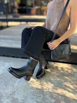Bota corta de cuero negro con punta cuadrada y taco bloque de altura media con textura grabada. Presenta un diseño minimalista con costura central vertical y cierre lateral interno.