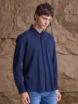 Camisa de manga larga color azul marino, con cuello clásico, cierre frontal de botones y un bolsillo en el pecho.