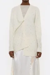 Cárdigan color crema de corte recto, con escote en V pronunciado, manga larga, cierre frontal con botones y aplicaciones de piedras de colores.