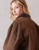 Campera de denim color marrón, con cuello de solapa en ecocuero negro. Cierre frontal con botones y bolsillos delanteros. Forro interno a tono.