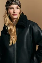 Campera tipo gamulán de cuero sintético negro, con interior y detalles de corderito sintético al tono en cuello y ruedo. Presenta cierre frontal metálico y diseño de silueta relajada.