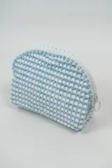 Neceser con textura de micropuntos en relieve, color celeste y blanco. Tiene forma rectangular con cierre superior de cremallera blanca.