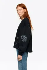 Sudadera negra de corte holgado y manga larga abullonada, con cuello redondo. Presenta detalles de pedrería brillante y estampados sutiles distribuidos por la prenda.