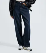 Pantalón baggy de jeans color azul oscuro, con tiro mediano, corte holgado y diseño de cinco bolsillos. Cuenta con cierre de cremallera y botón, y trabillas para cinturón.