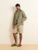Campera impermeable gris con capucha, cierre frontal y bolsillos laterales con cremallera.