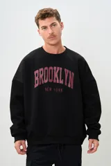 Buzo negro de corte holgado con estampa frontal de letras en color borgoña que dice "BROOKLYN" y "NEW YORK".