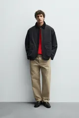 Parka de corte relajado en color negro, confeccionada en tejido de algodón con interior ligeramente acolchado. Presenta cuello de solapa en pana, cierre frontal con cremallera y bolsillos delanteros tipo plastrón con solapa y botones a presión.