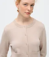 Cardigan de punto color beige, de corte clásico y manga larga, con cuello redondo, cierre frontal por botones y bolsillos delanteros funcionales.