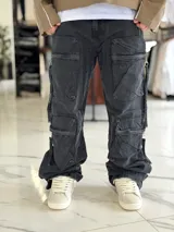 Pantalón cargo de jean negro con efecto acid wash, corte oversize, tiro medio y múltiples bolsillos laterales con solapa y cierres colgantes.