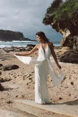 Vestido largo blanco de cuello halter con escote en V pronunciado, detalle de nudo drapeado en el delantero y tirantes decorados con cuentas esféricas.