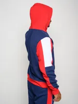 Canguro de felpa Umbro del Club Nacional de Football, con diseño tricolor en rojo, azul y blanco. Presenta capucha con cordones ajustables, bolsillo tipo canguro frontal, logo de la marca y escudo del club bordados en el pecho.