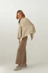 Ruana de tejido de punto industrial, confeccionada en lana fina sin teñir, con terminación en contraste de color y sistema de doble ojal para ajuste frontal.