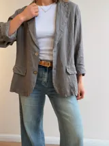 Blazer de lino color beige, de corte relajado y líneas clásicas. Presenta cuello con solapas, cierre frontal con dos botones y bolsillos con solapa en el frente.