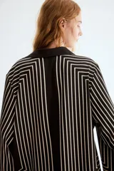 Camisa de corte oversized en tejido negro con leve brillo y diseño de líneas geométricas en color blanco. Cuenta con cuello clásico, cierre frontal de botones y mangas largas anchas.