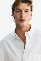 Camisa Oxford de algodón blanca, de corte regular fit, con cuello americano, bolsillo frontal aplicado y mangas largas con puños abotonados.