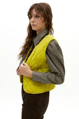 Chaleco capitoneado de terciopelo de seda, con cuello a la base y diseño sin mangas. Presenta un acabado acolchado con costuras onduladas y un tono amarillo vibrante.