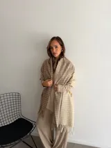 Bufanda de tejido suave con diseño de cuadros grandes en tonos negro y beige, terminada con flecos en los extremos.