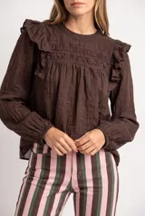 Blusa de color arena, con mangas largas y volados en los hombros. Presenta detalles de costuras fruncidas en el pecho y encaje.