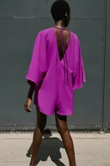 Mono corto de color fucsia, con escote en pico delantero y en la espalda, mangas anchas y largas, y detalle de fornitura dorada en el escote delantero con tiras finas para atar en la espalda.